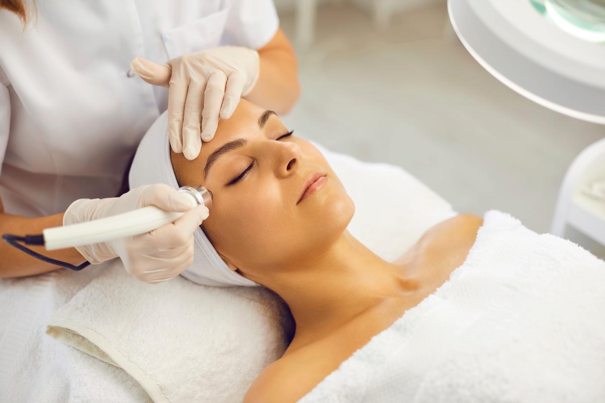 Relaxed young woman with eyes closed getting procedure of vacuum facial cleaning from cosmetologist in gloves in beauty spa salon. Facial treatment, skincare, cosmetology concept