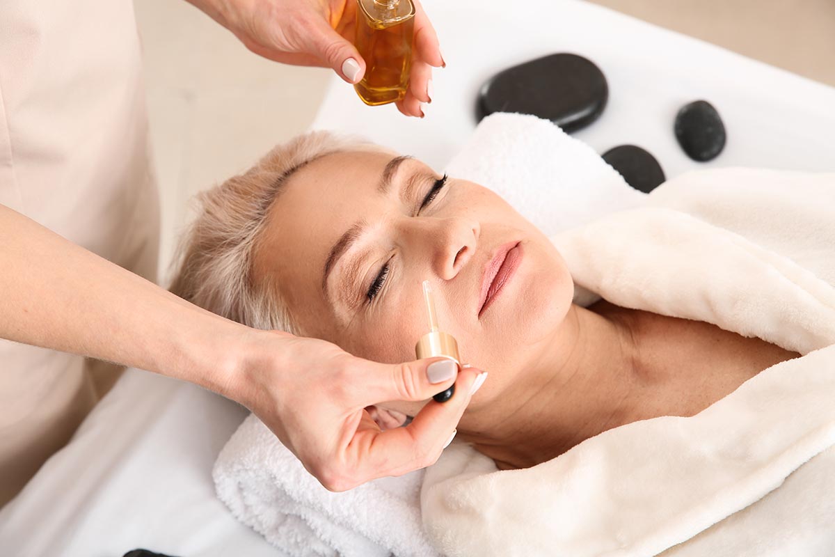 Mature woman undergoing treatment with face serum in beauty salon